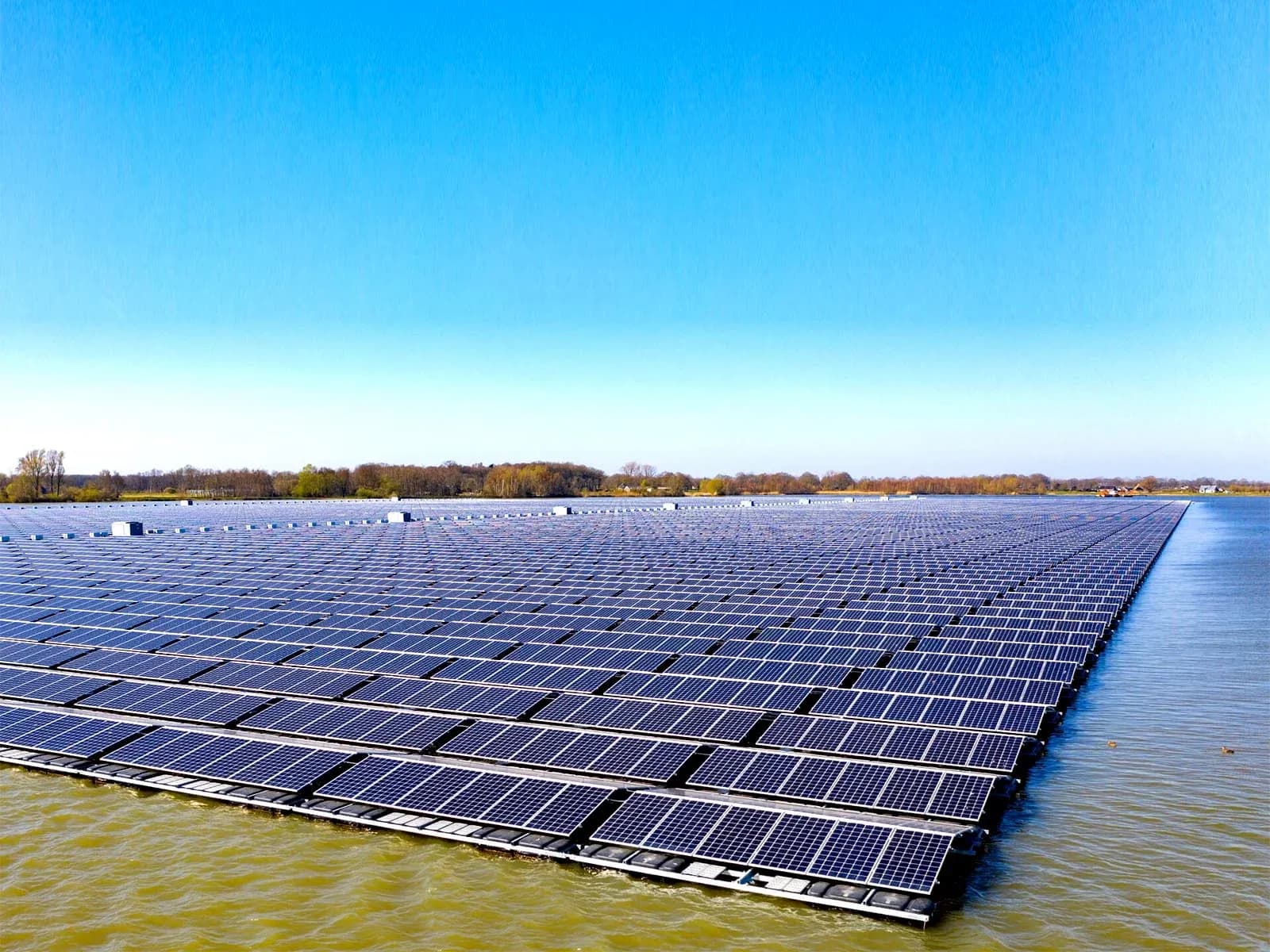 Rijen drijvende zonnepanelen op een wateroppervlak onder een heldere blauwe lucht Rijen drijvende zonnepanelen die een waterpartij bedekken onder een heldere blauwe lucht