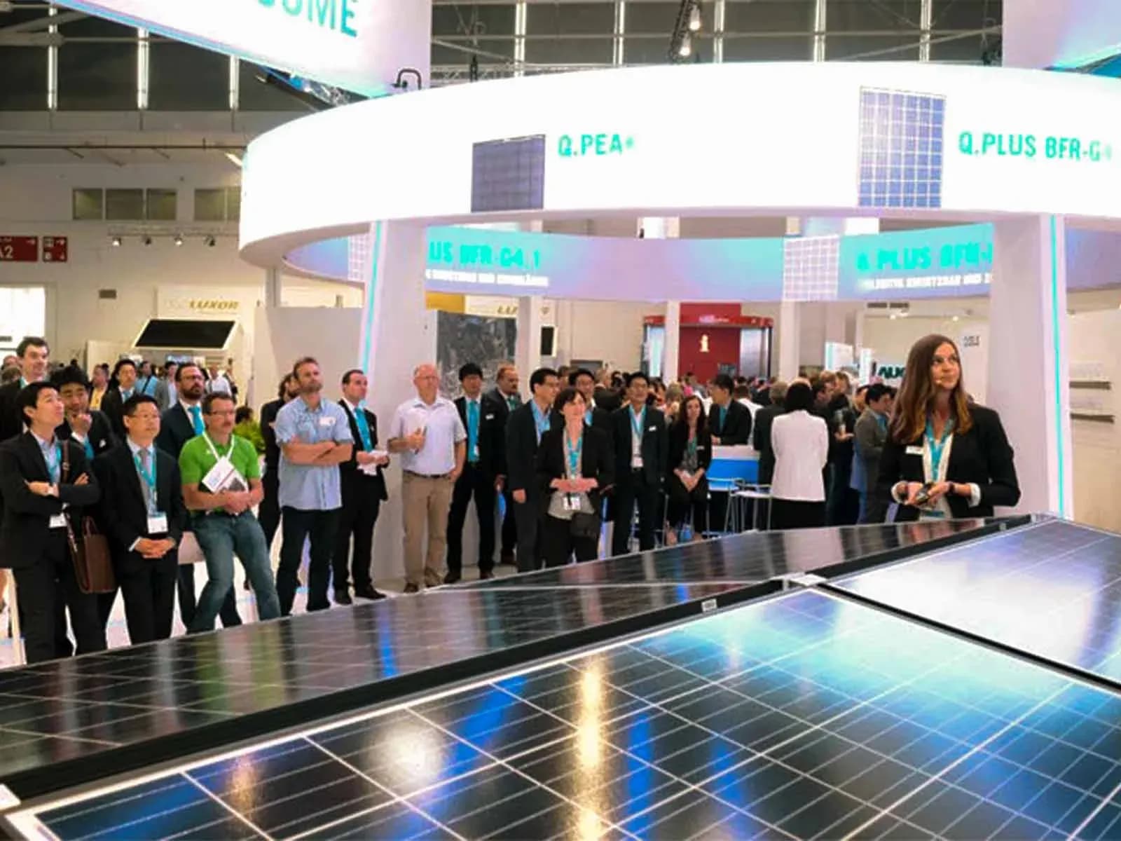 Besucher in einer Messehalle der Intersolar Europe vor einem Messestand mit Solarmodulen im Vordergrund