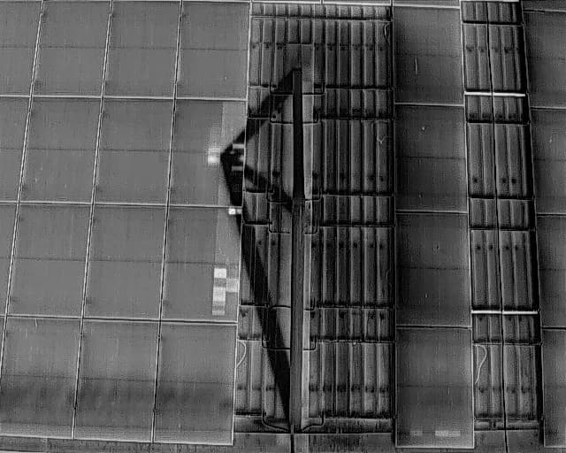 Vista térmica en escala de grises de paneles solares en una cubierta, con la sombra de una estructura sobre el conjunto Imagen térmica de módulos fotovoltaicos con diferencias de temperatura