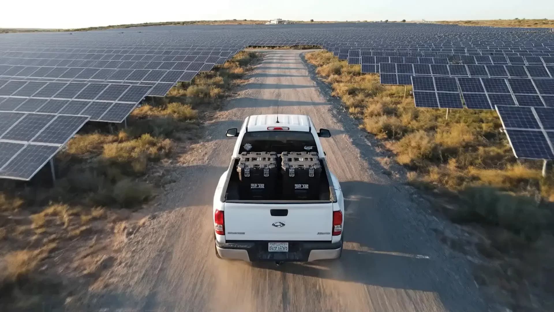 Camioneta con maletas de equipo circulando entre filas de paneles de una planta solar Camioneta con maletas de equipo circulando entre filas de paneles de una planta solar