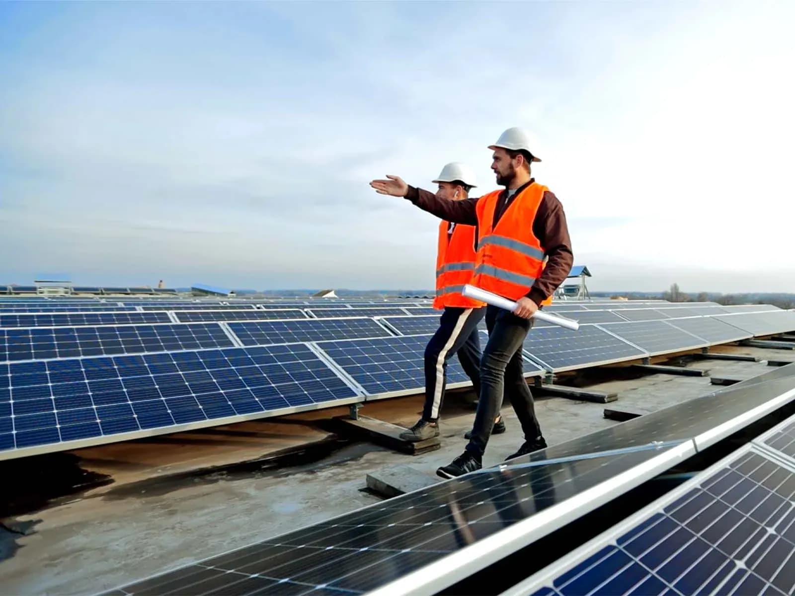 Two workers in safety vests and helmets standing among rooftop solar panels