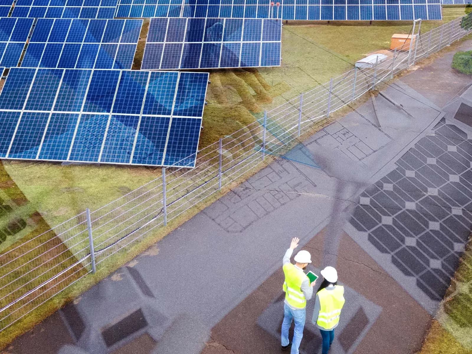 Aerial view of two workers beside a fenced solar array, with one pointing upward