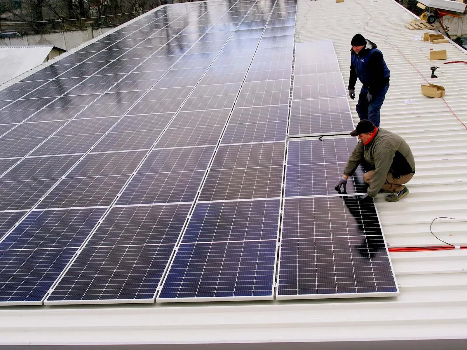 Two workers beside solar panels on a corrugated roof Solar power plant management